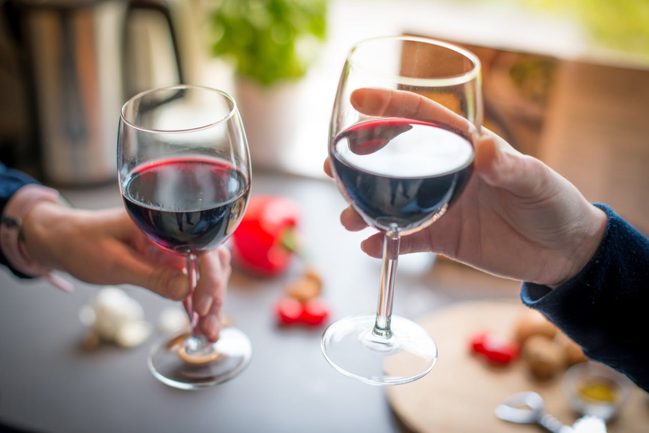 Two people toasting with red wine glasses on a dining table indoors.