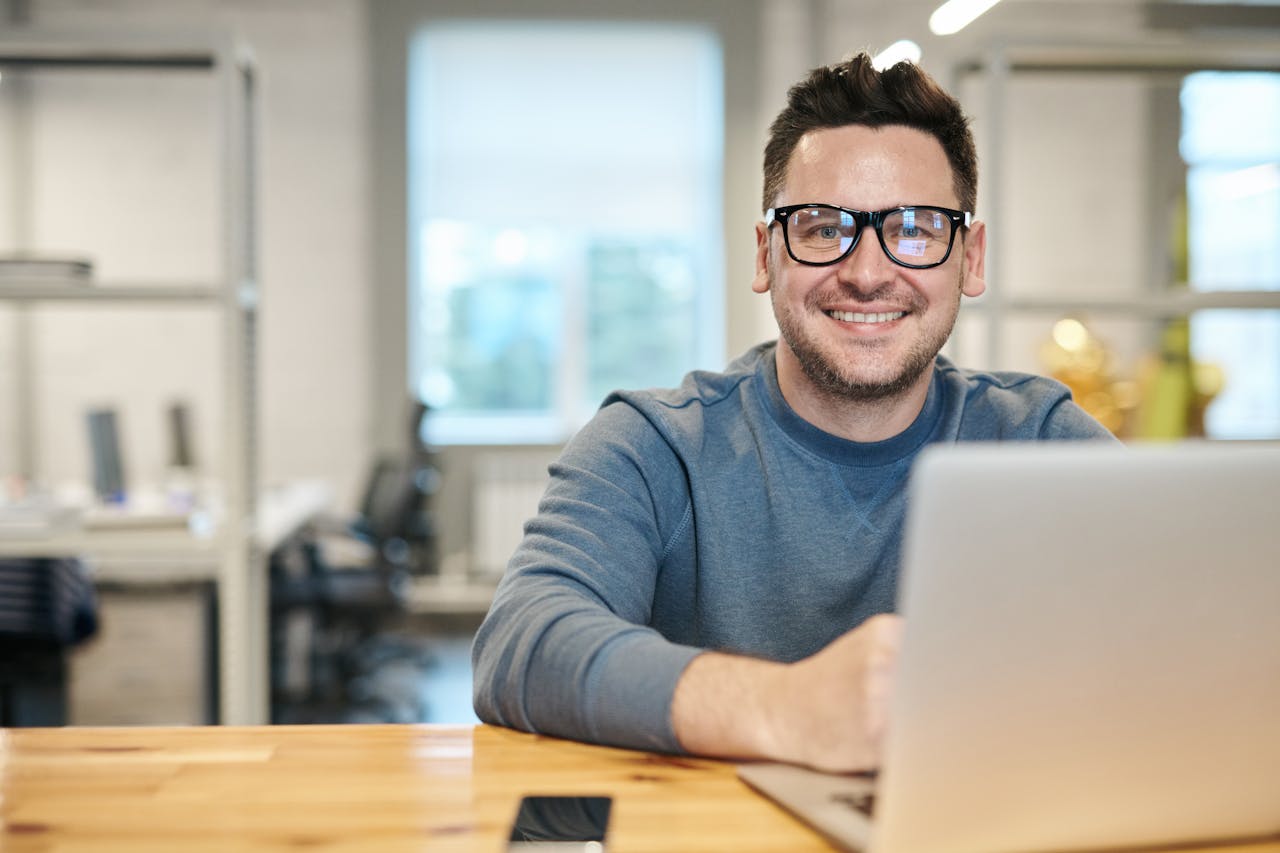 about-header Happy man wearing glasses working remotely on laptop in modern office environment.